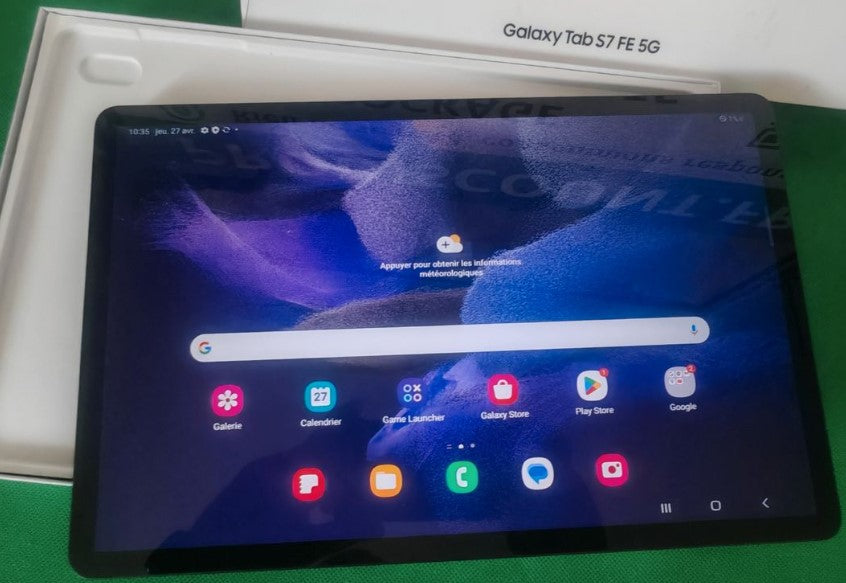 Samsung Galaxy Tab S7 FE 5G allumée, écran d'accueil, devant sa boîte